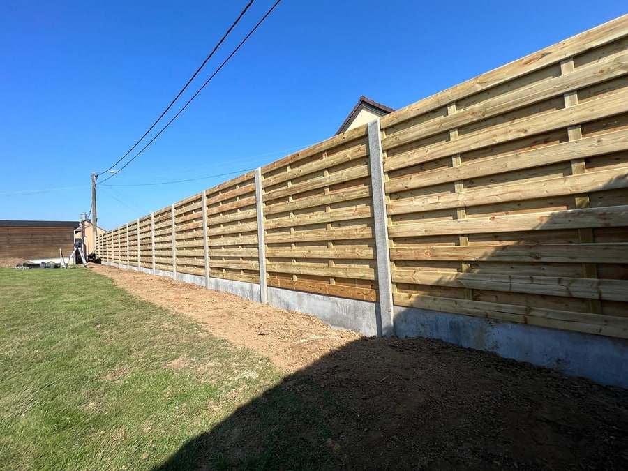 Houten schutsels met gevlochten horizontale planken tussen betonnen palen, onder een blauwe hemel