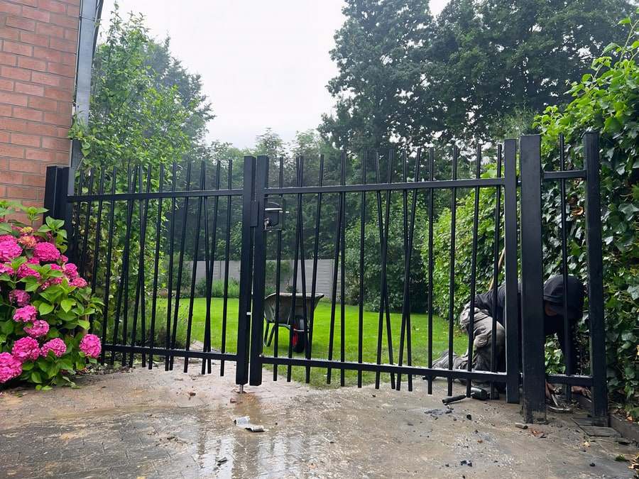 Zwarte stalen dubbele draaipoort op maat, met sierspijlen, tijdens plaatsing bij een woning
