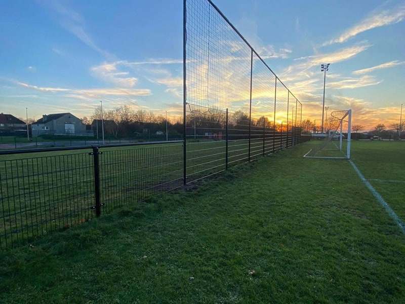 Hoge zwarte draadafsluiting rond een sportterrein met grasveld en doelen