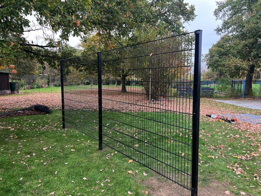 Zwarte staalmatten afsluiting met vierkante palen in een tuin met herfstbladeren