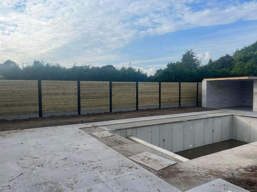 Tand- en groefhekwerk met horizontale planken tussen zwarte palen rond een tuin in aanleg